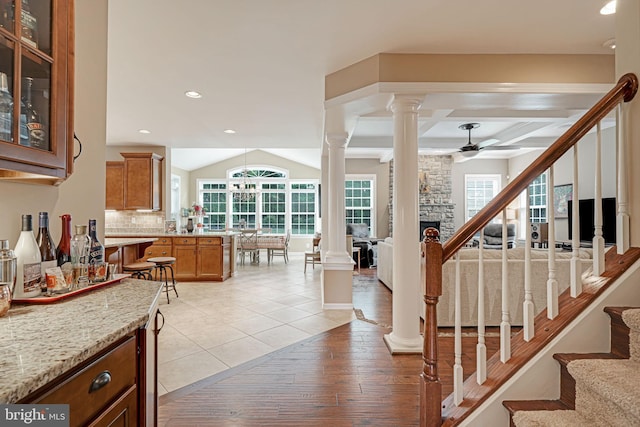 interior space with decorative columns, a ceiling fan, a stone fireplace, stairway, and a wealth of natural light