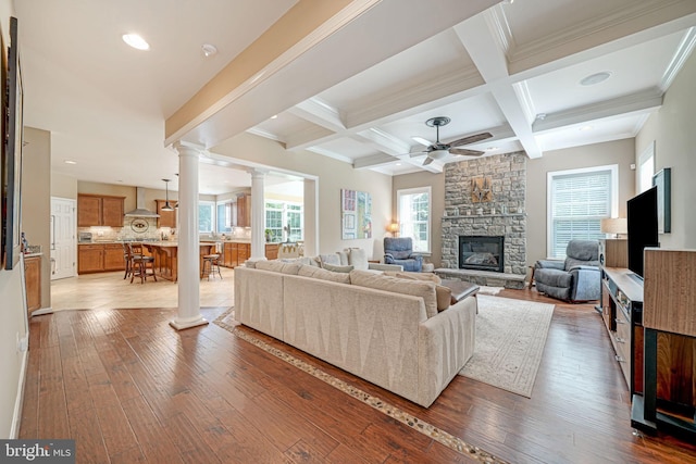 living area with wood-type flooring, ornate columns, beamed ceiling, and a fireplace