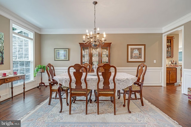 dining space with an inviting chandelier, ornamental molding, dark wood-type flooring, and a wainscoted wall