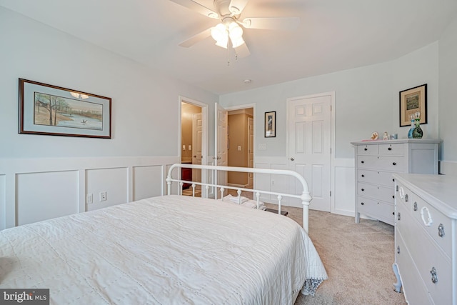 bedroom with ceiling fan, light colored carpet, wainscoting, a closet, and a decorative wall