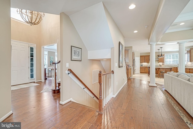 entryway featuring ornate columns, baseboards, a chandelier, and light wood finished floors