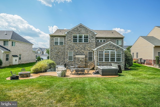back of house featuring a lawn, a hot tub, a patio, a fire pit, and stone siding