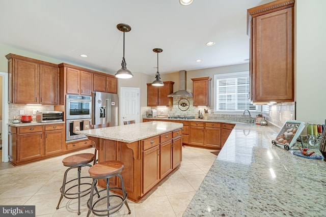 kitchen with wall chimney range hood, a kitchen island, tasteful backsplash, light stone counters, and stainless steel appliances