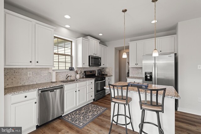 kitchen featuring white cabinets, dark wood-style flooring, appliances with stainless steel finishes, a sink, and a center island