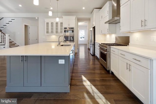 kitchen featuring wall chimney range hood, high quality appliances, a spacious island, a sink, and white cabinets