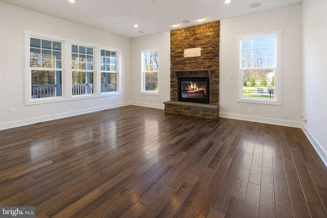 unfurnished living room featuring a healthy amount of sunlight, baseboards, dark wood-style flooring, and a stone fireplace