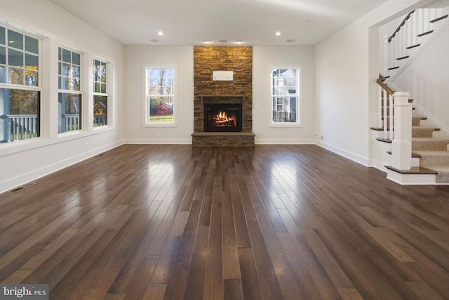 unfurnished living room with a fireplace, plenty of natural light, stairway, and dark wood-type flooring