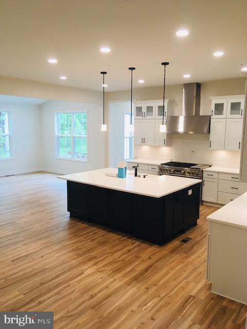 kitchen featuring light wood-style floors, light countertops, wall chimney exhaust hood, and white cabinetry