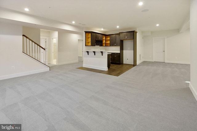 unfurnished living room with wet bar, stairs, carpet floors, baseboards, and recessed lighting