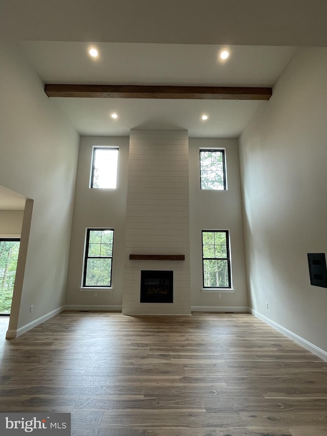unfurnished living room with beamed ceiling, a wealth of natural light, and wood finished floors