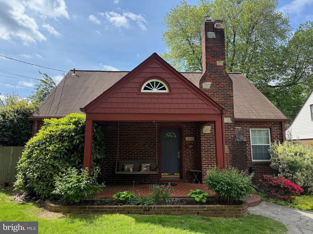 view of front of property featuring covered porch, a chimney, and brick siding