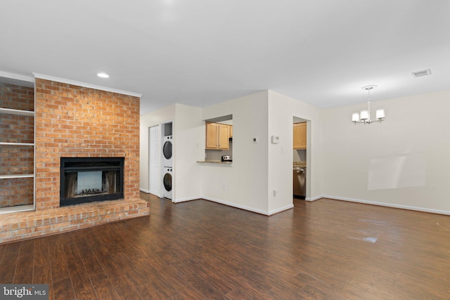 unfurnished living room featuring stacked washer and clothes dryer, dark wood-style flooring, a chandelier, baseboards, and a brick fireplace