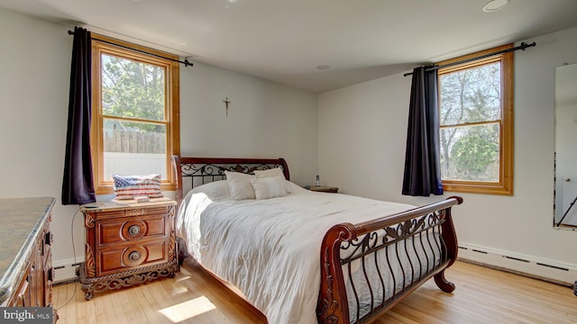 bedroom with multiple windows, a baseboard heating unit, and light wood-style flooring