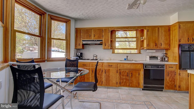 kitchen with a sink, light countertops, light tile patterned floors, black appliances, and under cabinet range hood