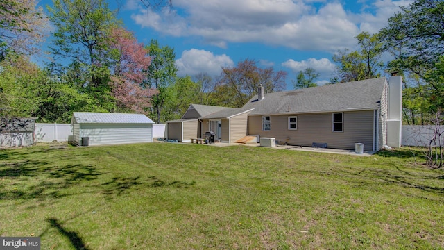 rear view of house with a chimney, a lawn, an outbuilding, a patio area, and a fenced backyard