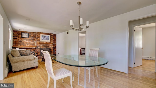 dining area with light wood-type flooring, a baseboard radiator, a chandelier, and a fireplace