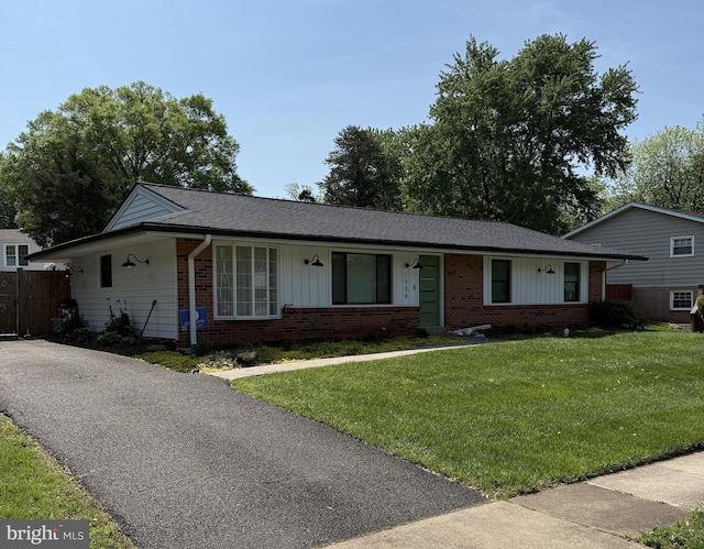 ranch-style home featuring brick siding, a shingled roof, fence, and a front yard