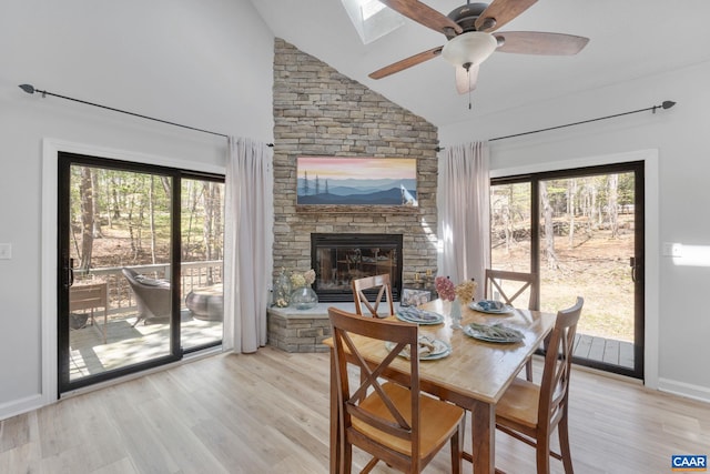 dining area featuring plenty of natural light, a ceiling fan, light wood finished floors, and a stone fireplace