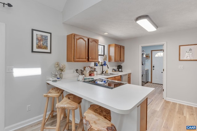 kitchen with a sink, light countertops, baseboards, light wood finished floors, and a breakfast bar