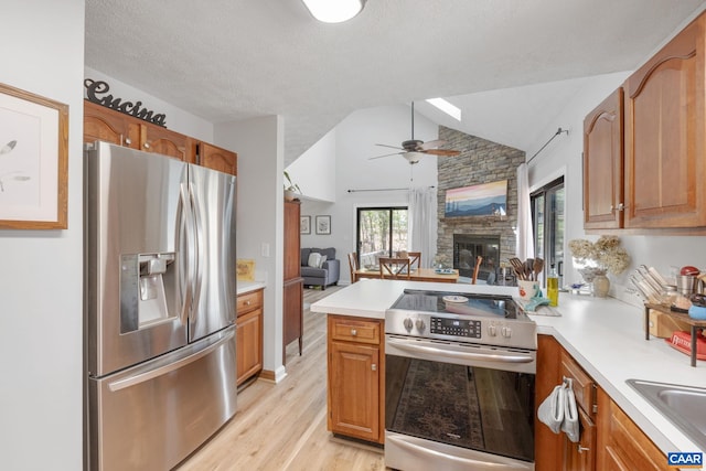 kitchen featuring a peninsula, open floor plan, vaulted ceiling with skylight, light wood finished floors, and stainless steel appliances