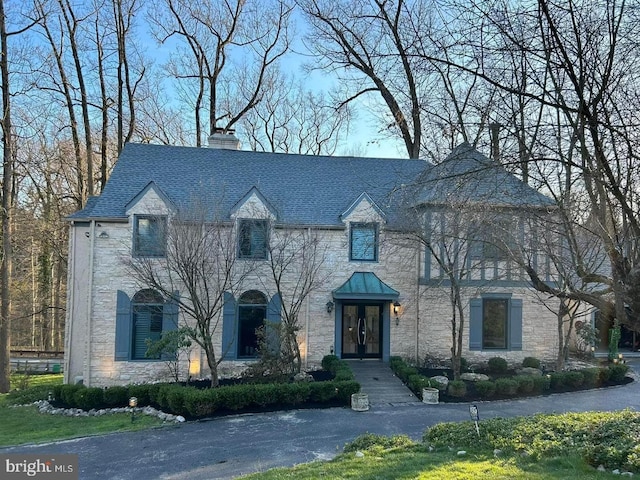 french country inspired facade featuring french doors, stone siding, and a chimney