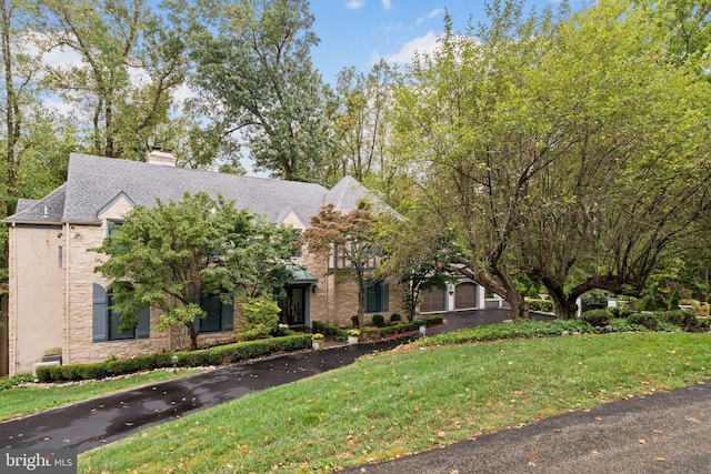 view of front of property featuring a shingled roof, a front lawn, stone siding, and a chimney