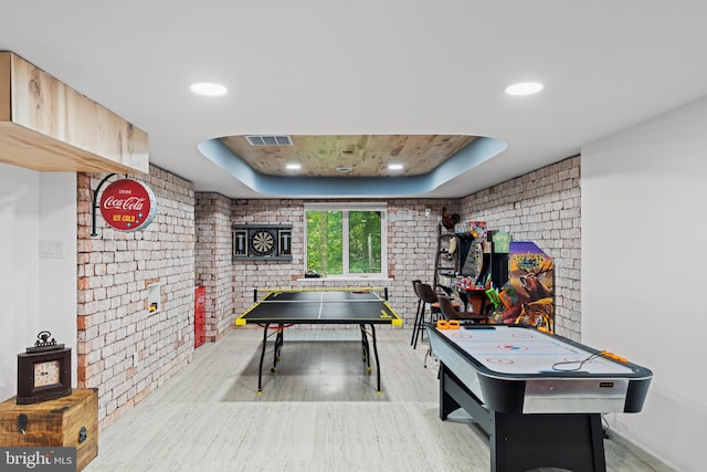 rec room featuring visible vents, wood finished floors, brick wall, recessed lighting, and a tray ceiling