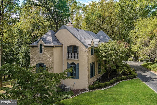 view of property exterior featuring stone siding, stucco siding, a chimney, a balcony, and a yard