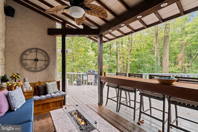 wooden deck featuring a ceiling fan, a view of trees, a grill, and an outdoor living space with a fire pit