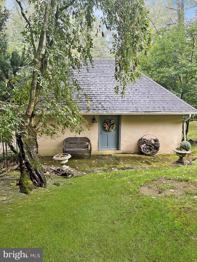 property entrance featuring a yard, roof with shingles, and stucco siding