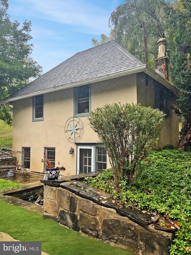back of property with a shingled roof, stucco siding, and a chimney