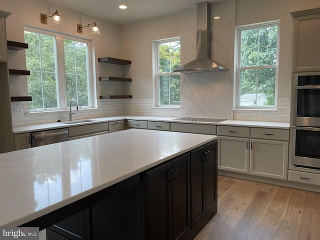 kitchen with a sink, appliances with stainless steel finishes, open shelves, and wall chimney range hood