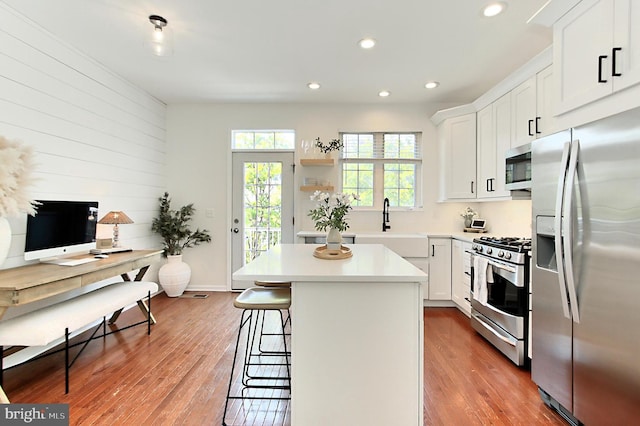 kitchen featuring appliances with stainless steel finishes, a kitchen breakfast bar, recessed lighting, wood finished floors, and a kitchen island