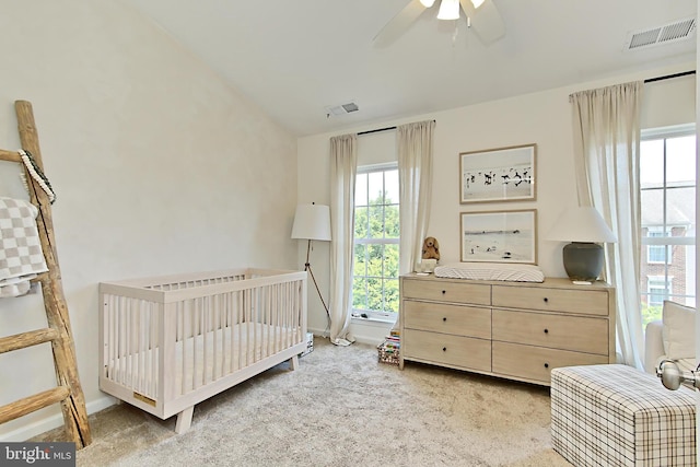 bedroom with light colored carpet, visible vents, multiple windows, and a crib