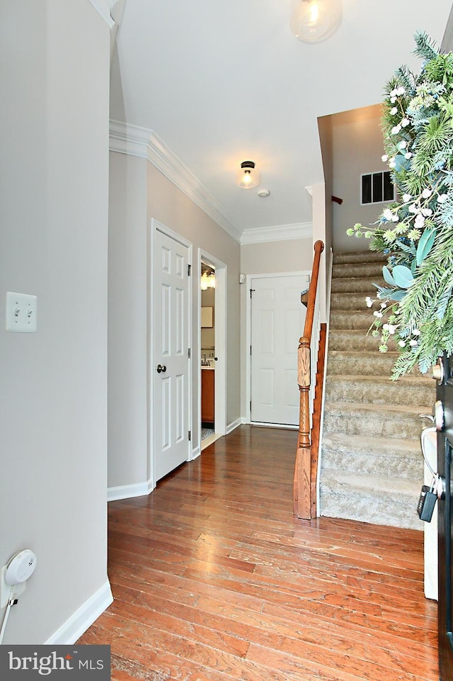 foyer entrance featuring visible vents, stairway, baseboards, wood-type flooring, and ornamental molding