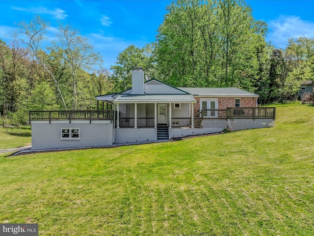 back of house featuring a wooden deck, a chimney, brick siding, metal roof, and a yard