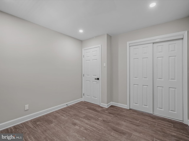 unfurnished bedroom with baseboards, a closet, recessed lighting, and wood finished floors