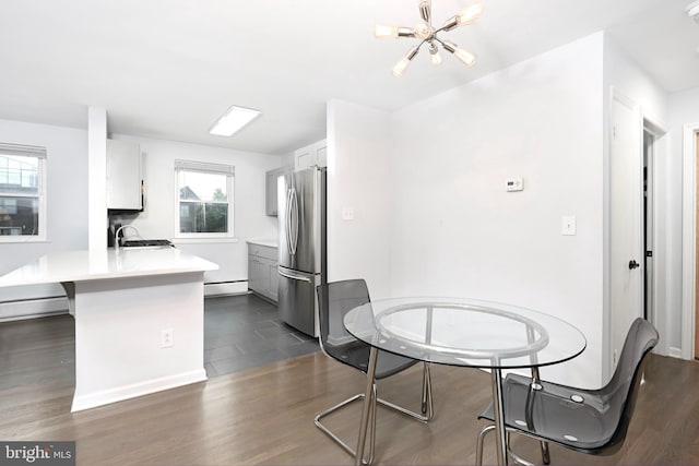 kitchen featuring freestanding refrigerator, a peninsula, a baseboard radiator, a chandelier, and a sink