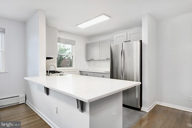 kitchen featuring freestanding refrigerator, a peninsula, a sink, and wood finished floors
