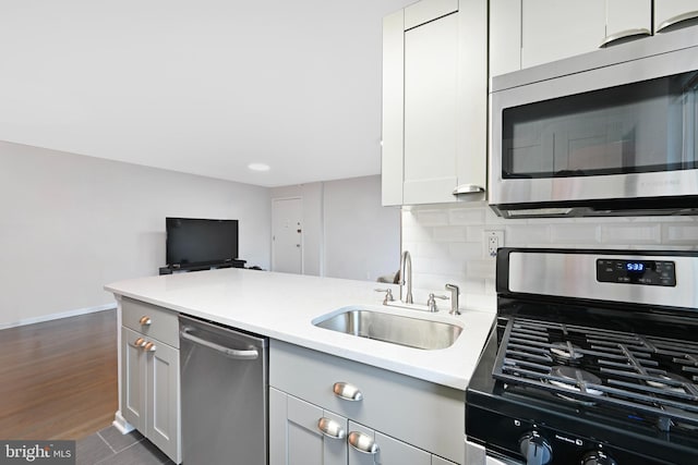 kitchen with a sink, light countertops, baseboards, a peninsula, and stainless steel appliances