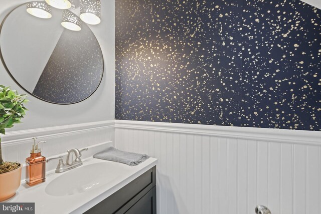 bathroom featuring vanity, a wainscoted wall, and wallpapered walls