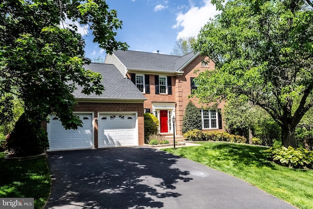 colonial home with roof with shingles, a front lawn, brick siding, a garage, and aphalt driveway