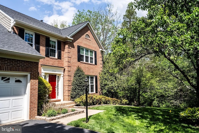 view of front of property featuring brick siding, a shingled roof, a front lawn, and an attached garage