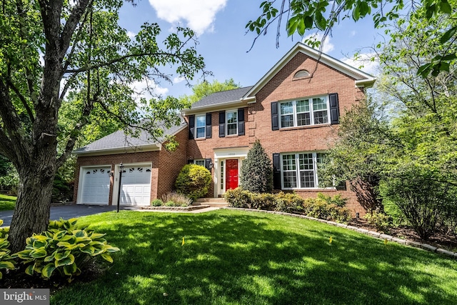colonial inspired home with brick siding, a garage, a front lawn, and aphalt driveway
