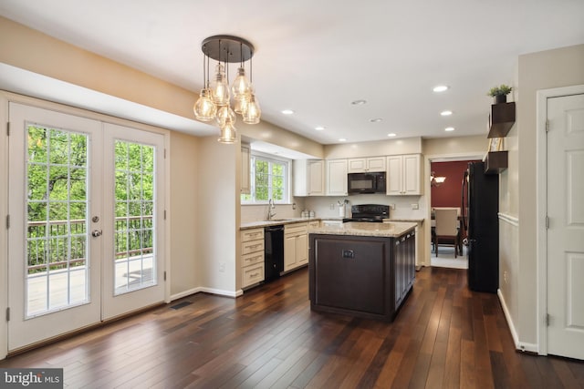 kitchen featuring light stone countertops, a sink, decorative light fixtures, a kitchen island, and black appliances