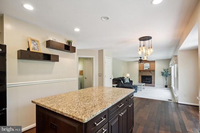 kitchen featuring ceiling fan, dark brown cabinetry, a kitchen island, dark wood-style flooring, and a fireplace