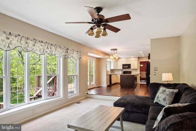 living area with baseboards, visible vents, ceiling fan with notable chandelier, and dark colored carpet