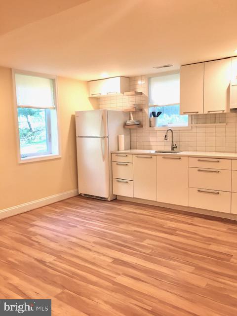 13211 Lutes Dr, Silver Spring, MD 20906 - kitchen featuring a sink, light wood-style flooring, freestanding refrigerator, and white cabinets