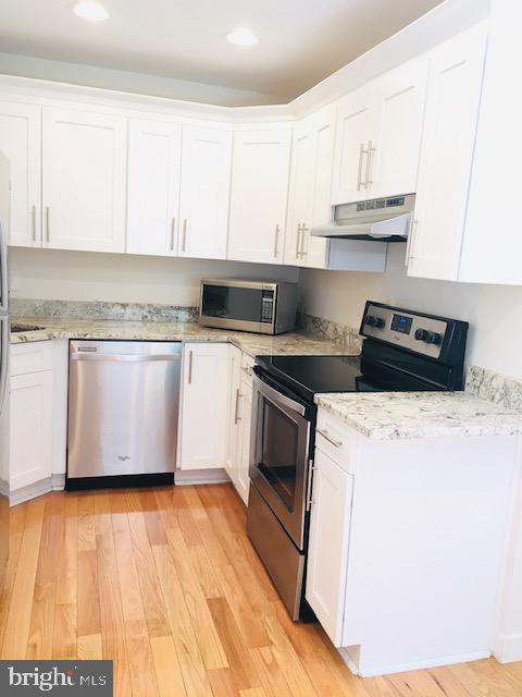 13211 Lutes Dr, Silver Spring, MD 20906 - kitchen featuring appliances with stainless steel finishes, under cabinet range hood, white cabinetry, light wood-type flooring, and recessed lighting