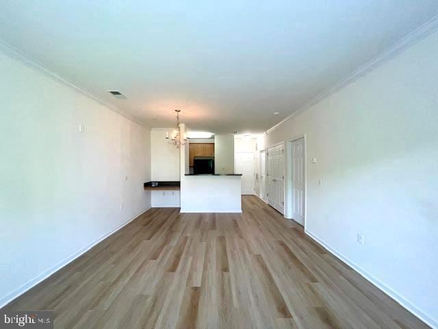 unfurnished living room featuring visible vents, crown molding, wood finished floors, baseboards, and a notable chandelier
